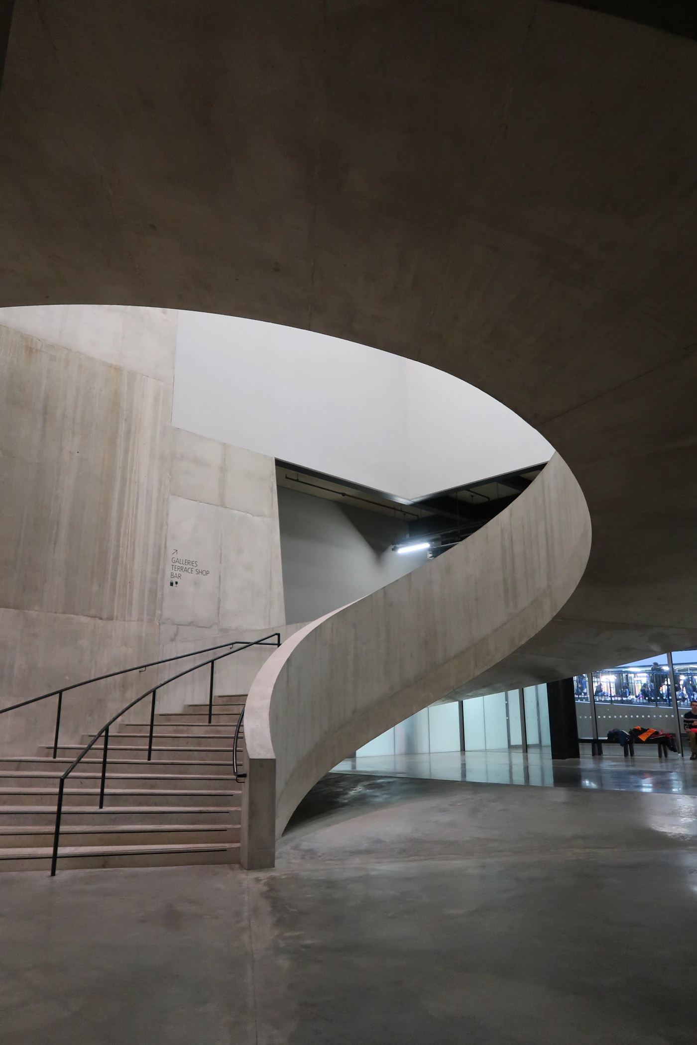 A sweeping concrete stair curves around a softly lit central opening