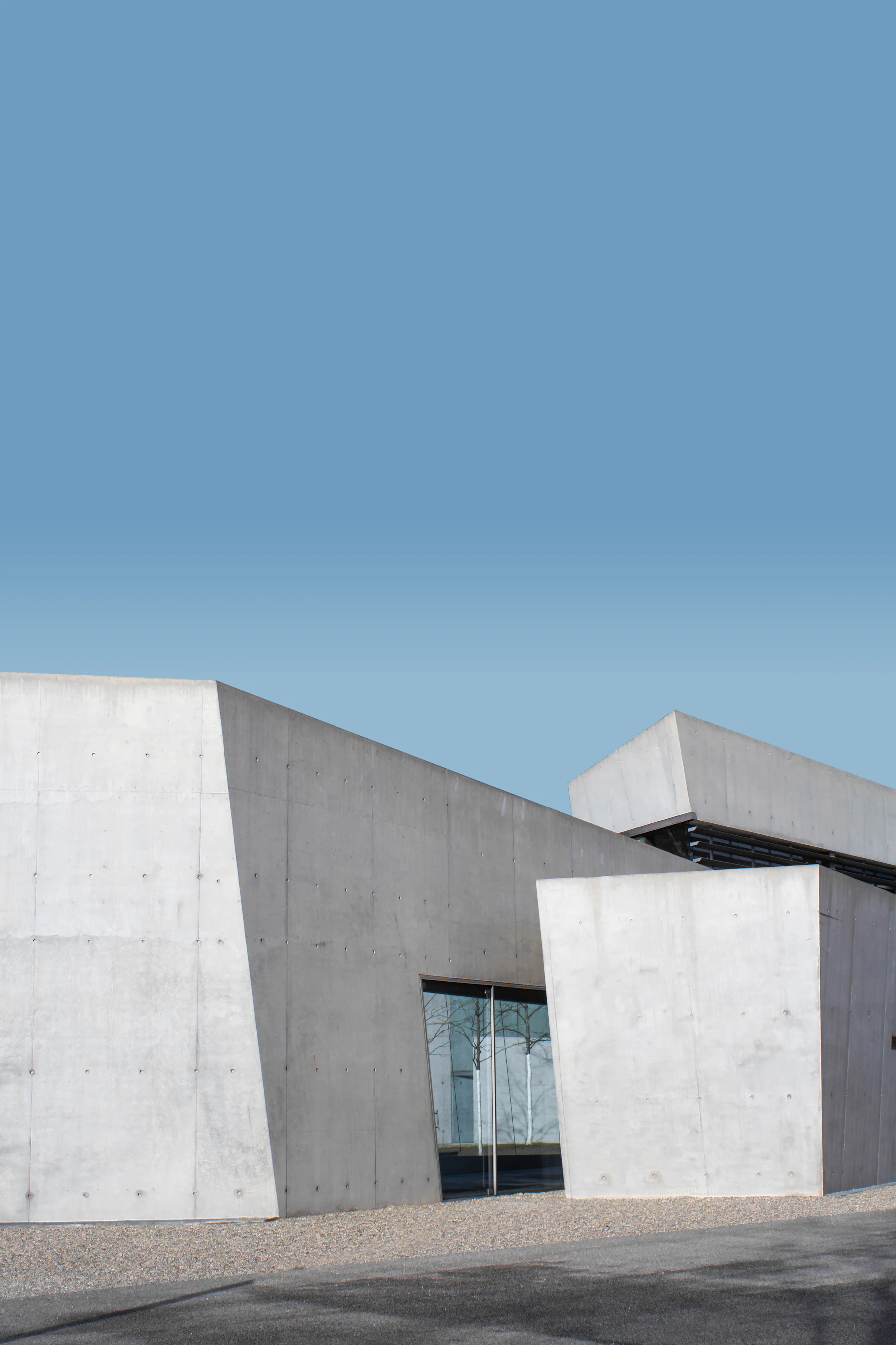 Angular pale concrete volumes sit beneath a clear blue sky