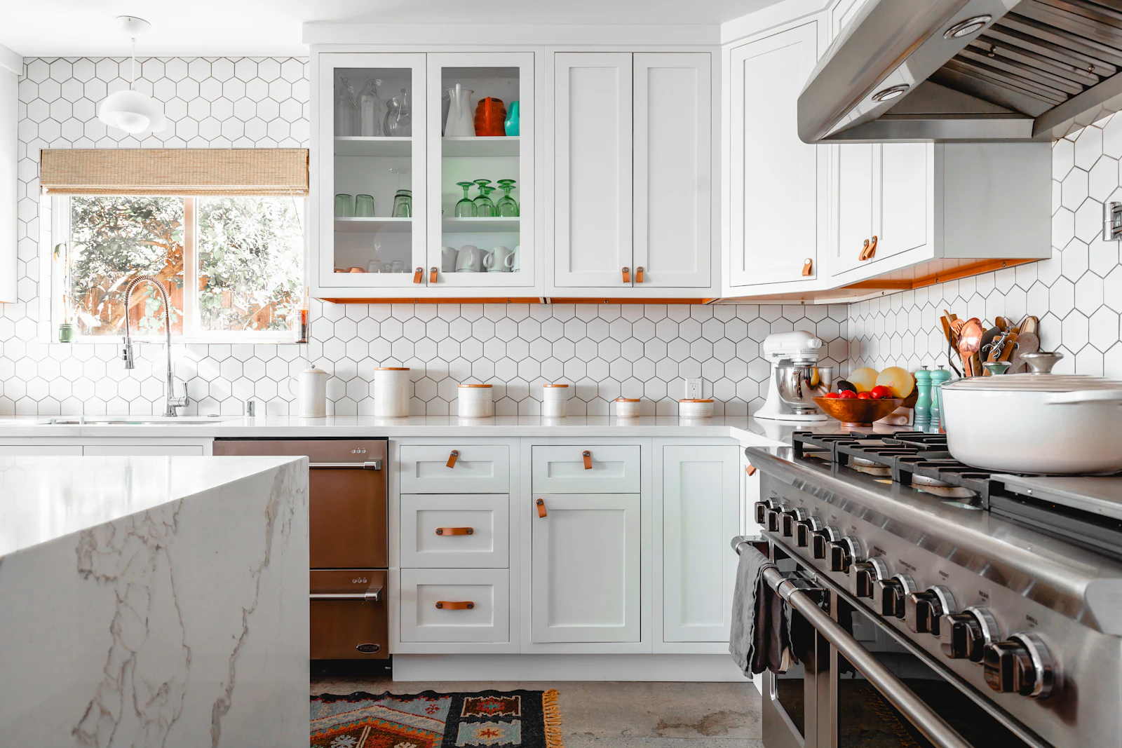 Bright kitchen with white cabinetry, hexagonal wall tiles, and warm copper-colored details