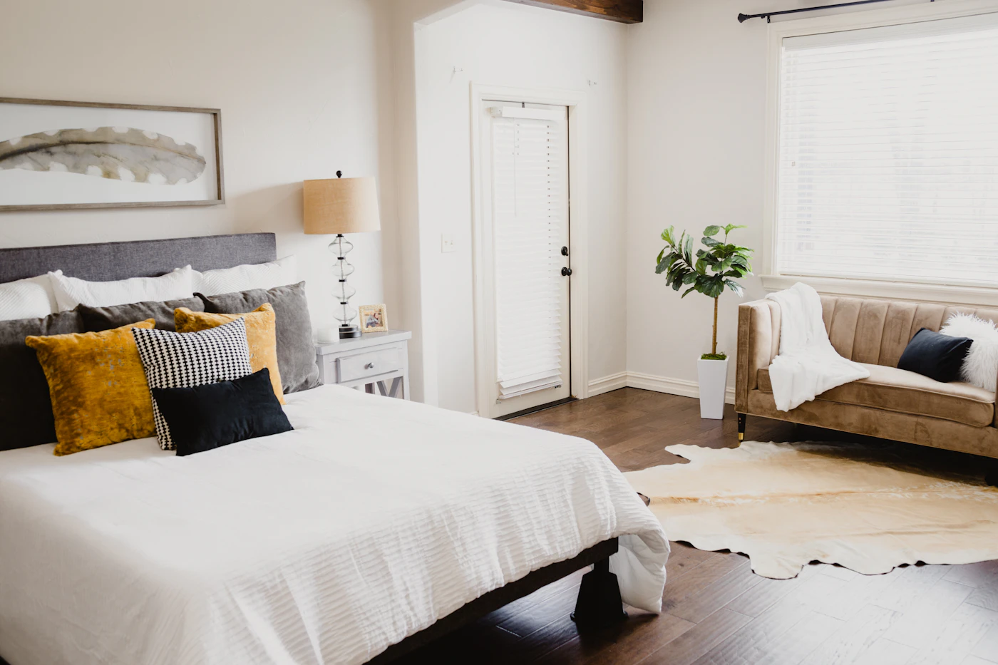 A bright bedroom with white linen, a soft sofa, and daylight through wide windows
