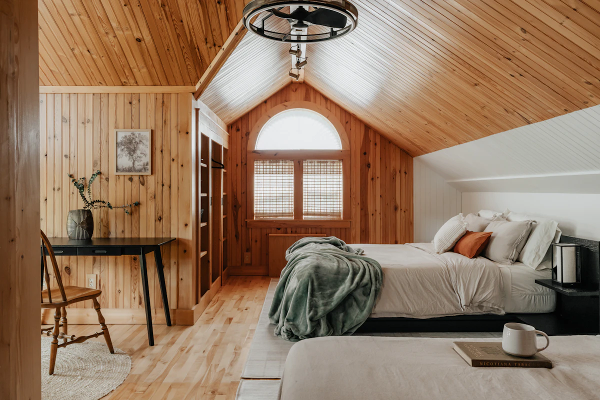 Warm timber walls, a sloping ceiling, and a bed dressed in white linen with a green throw