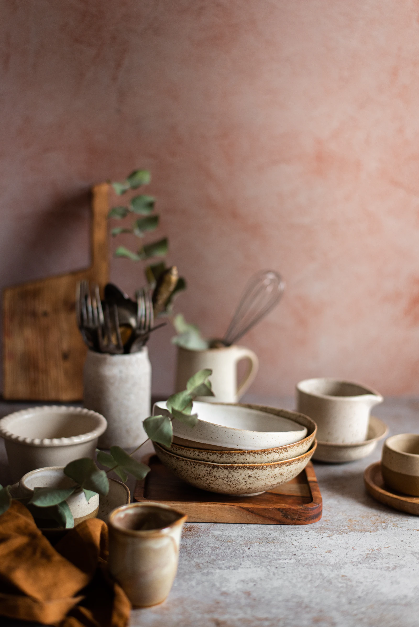 Neutral ceramic bowls, a cup, and kitchen utensils arranged on a softly lit tabletop