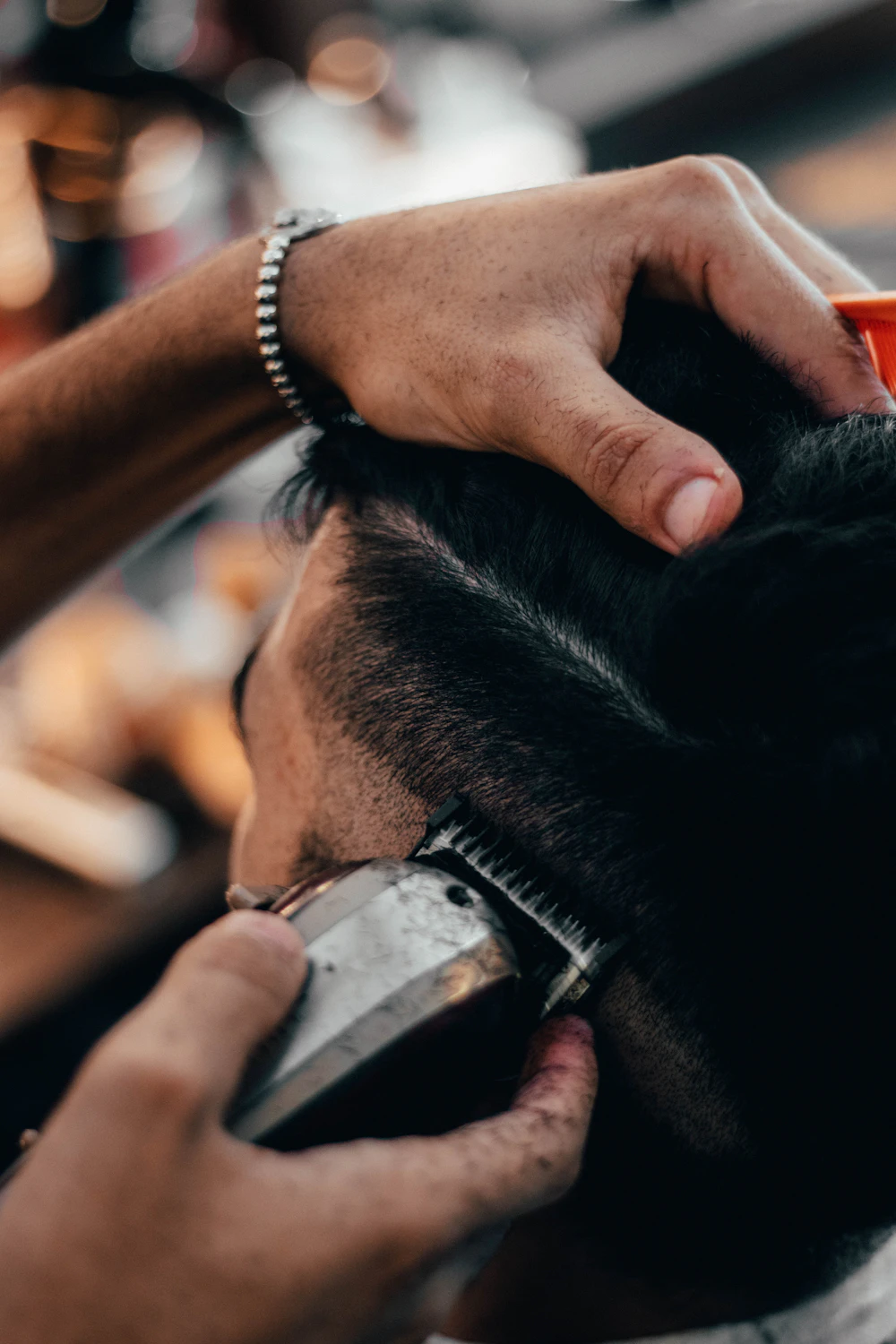 Hands using a clipper on short dark hair in a close crop
