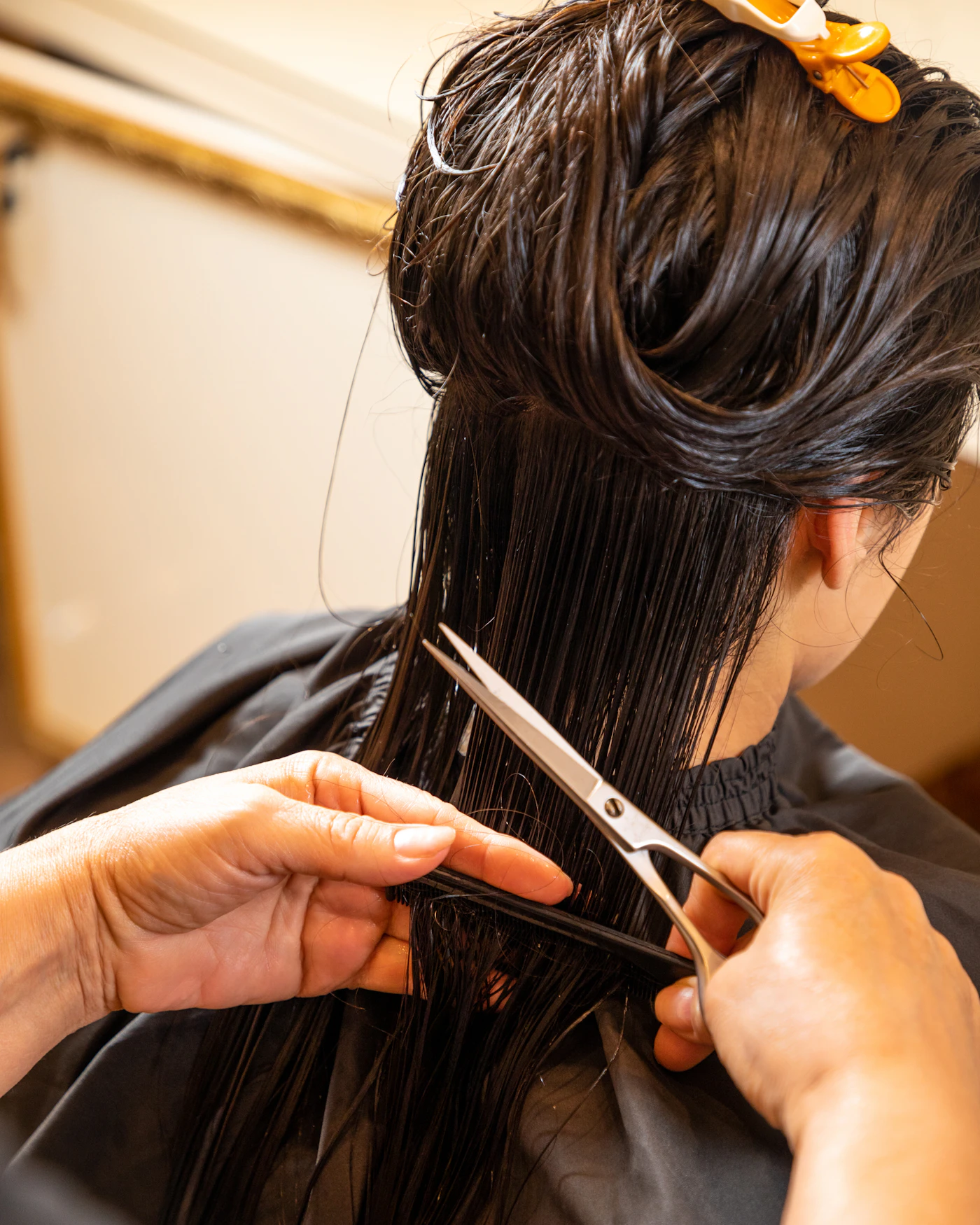 A close view of hands shaping a section of dark hair with scissors, seen from behind